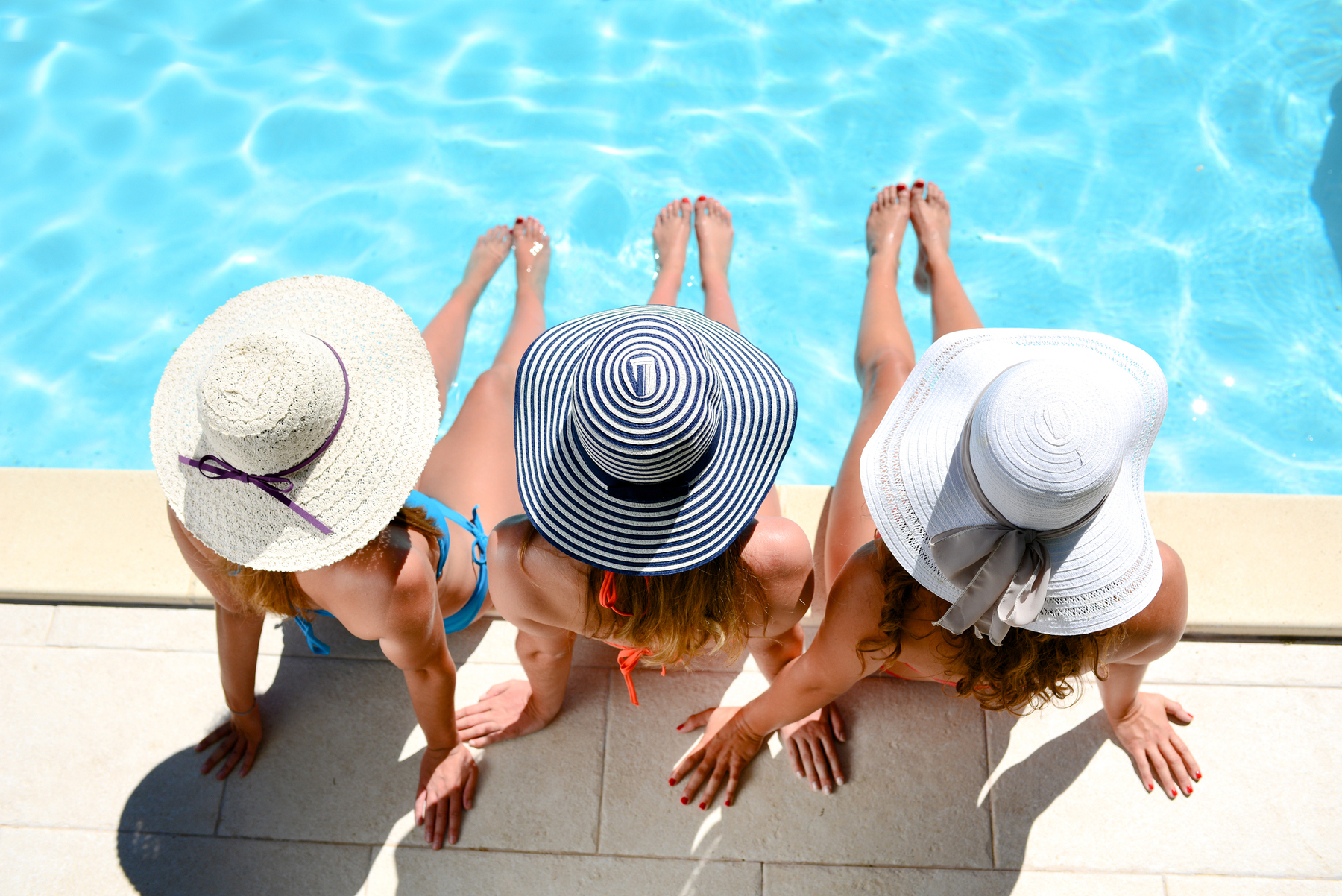 Three women in hats lounging by the pool