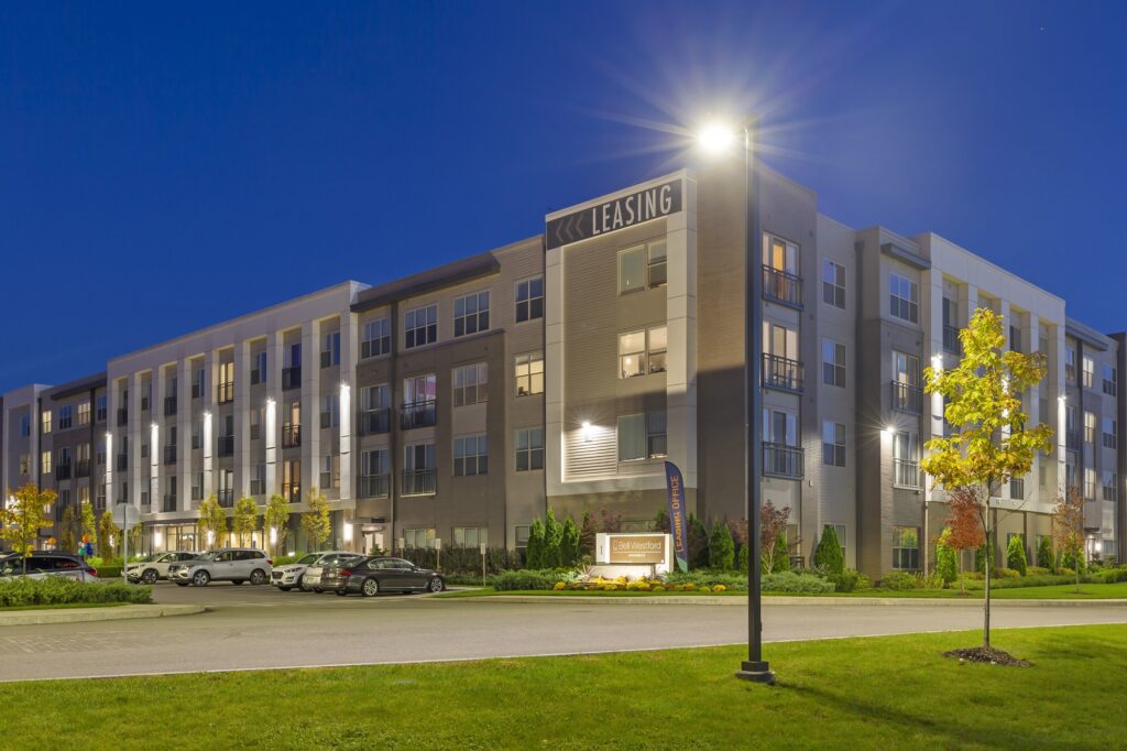 Exterior dusk shot of entrance to apartment complex with garden landscaping and street lamp