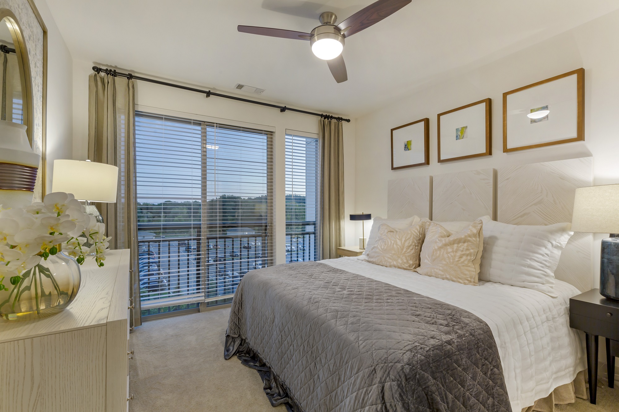 Bedroom with ceiling fan, large window, plush carpet, dresser, king sized bed and nightstands