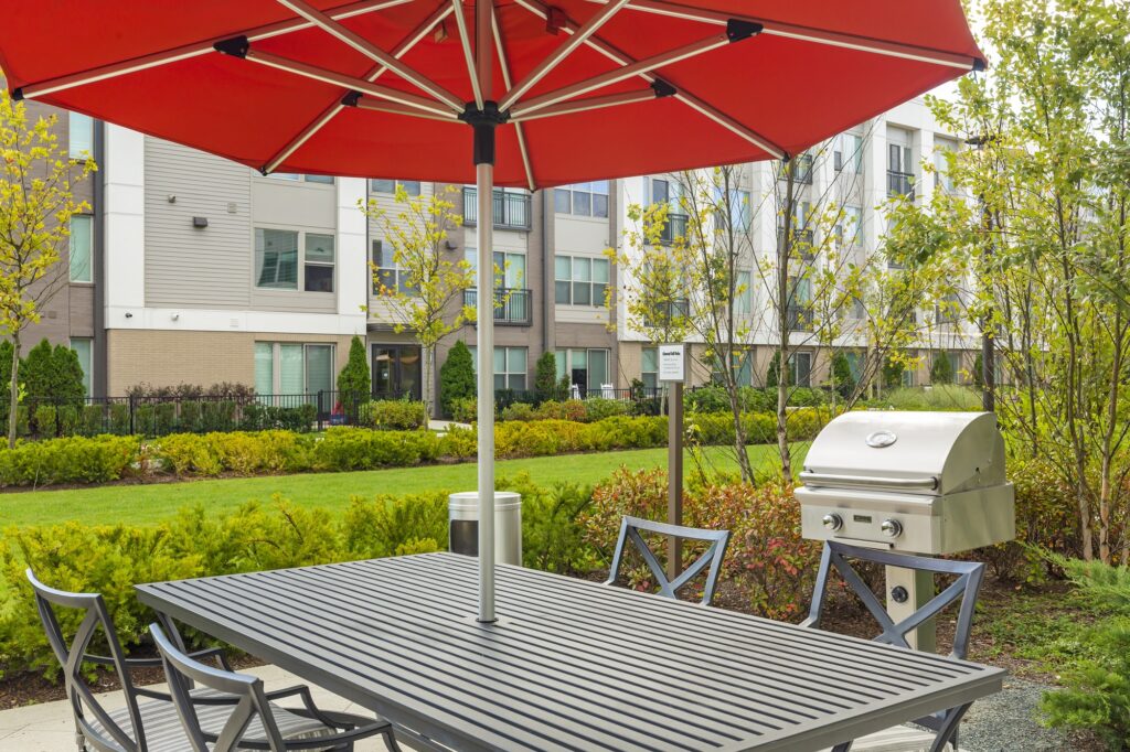Outdoor grilling station area with shaded seating, trees and garden landscaping