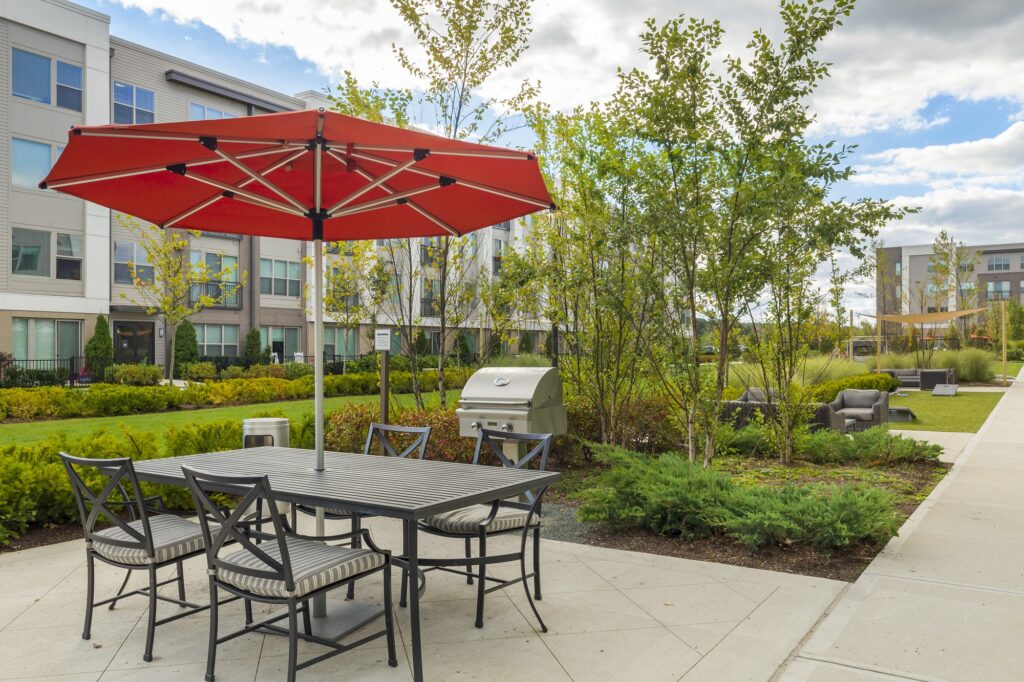 Outdoor grilling station area with shaded seating, trees and garden landscaping